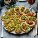 A gourmet appetizer platter featuring delicious bruschetta with sprouts, paired with a selection of wines.